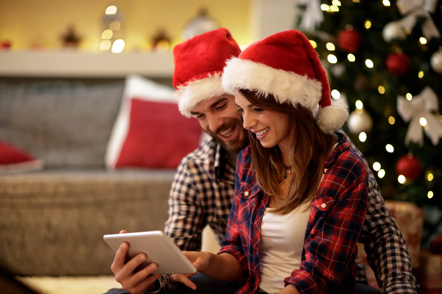 Zwei glückliche Menschen mit Weihnachtsmütze schauen auf einen Bildschirm
