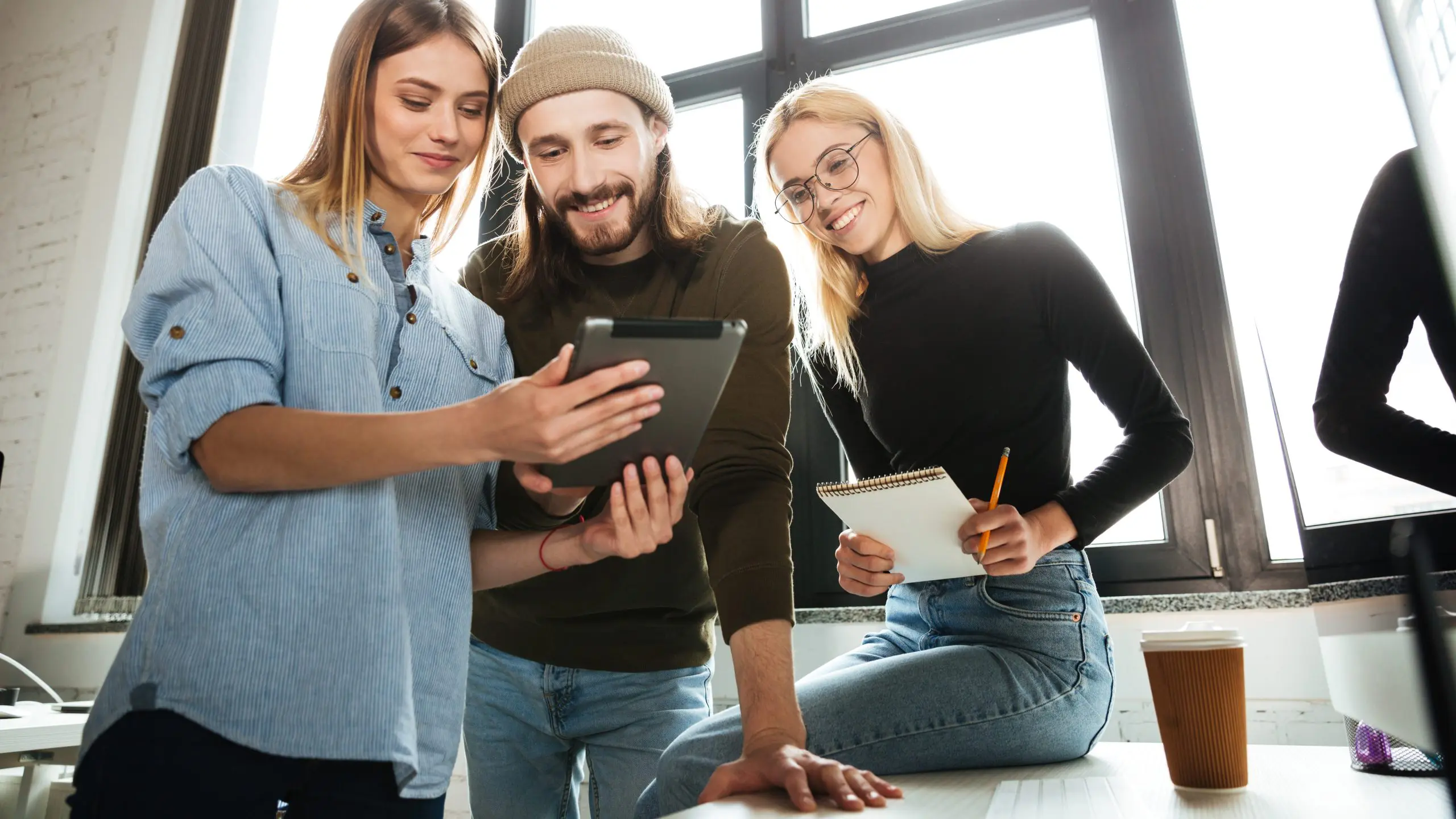 Ein junger Mann und zwei junge Frauen schauen gemeinsam auf ein Tablet.