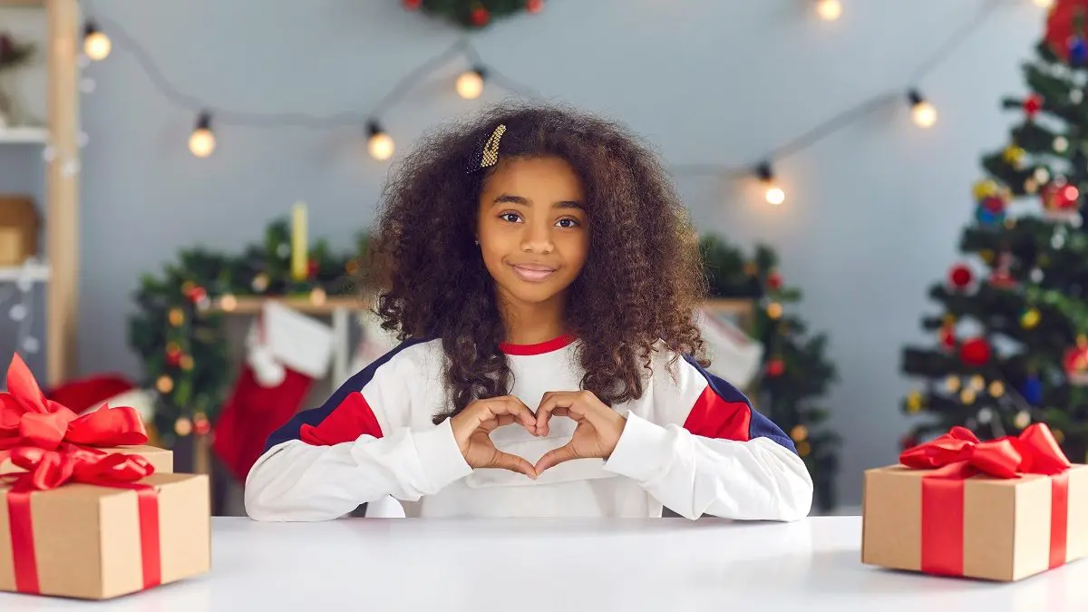 Mädchen zeigt Herz mit Händen an Tisch mit Weihnachtsdeko