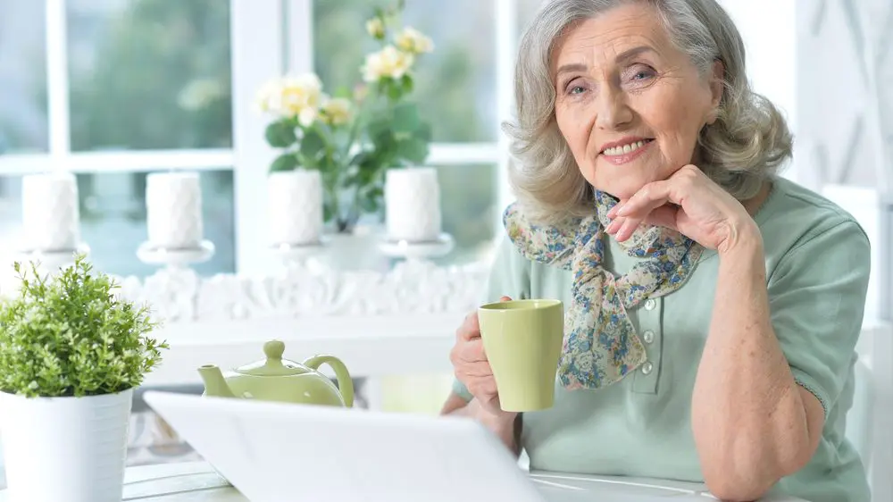 Seniorin sitzt lächelnd vor einem LapTop