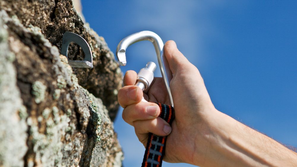 Bild einer Hand, die einen Sicherheits-Karabiner an einer Felswand einhängt