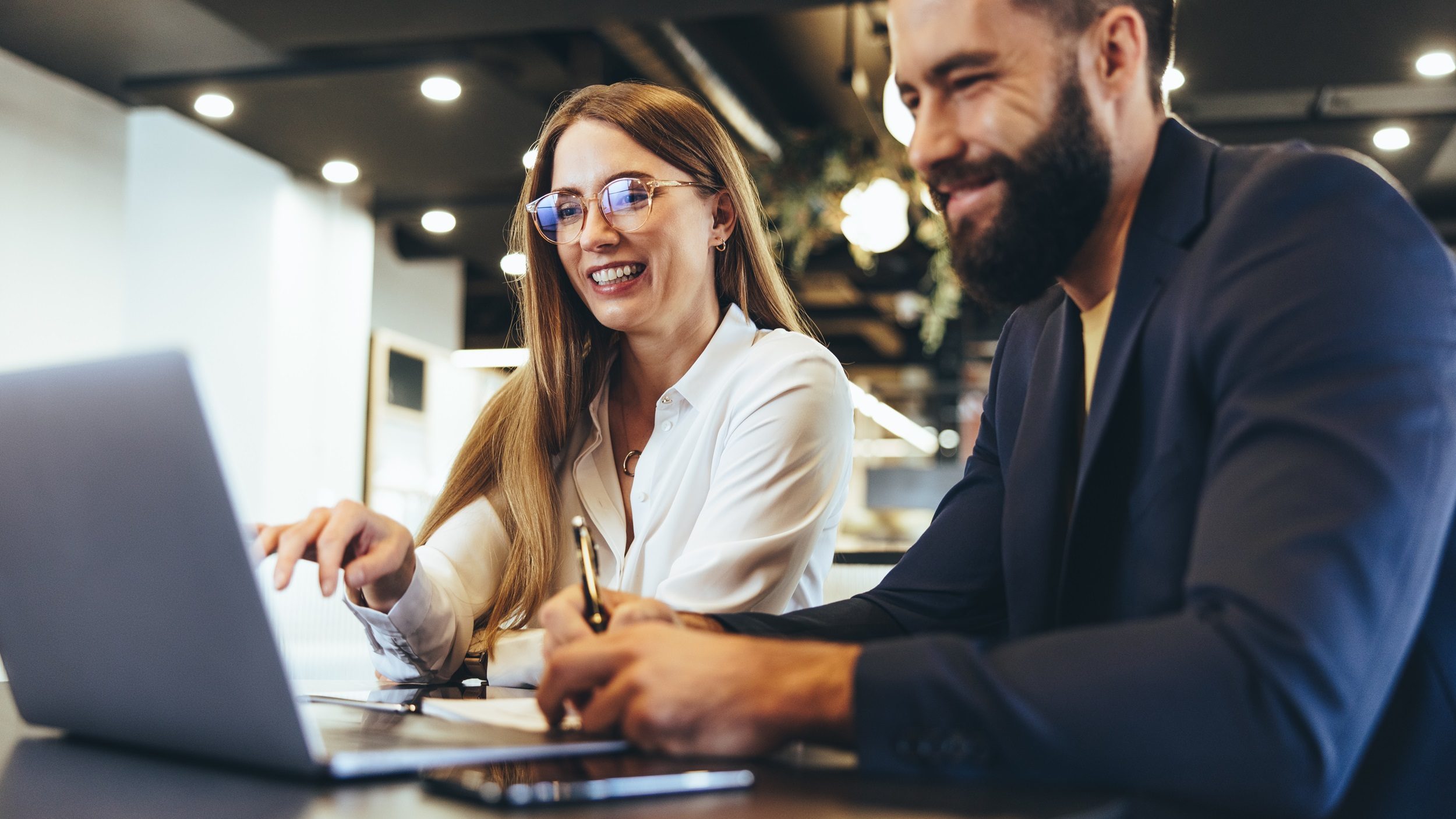 Eine junge Frau und ein junger Mann sitzen lächelnd vor einem Laptop.