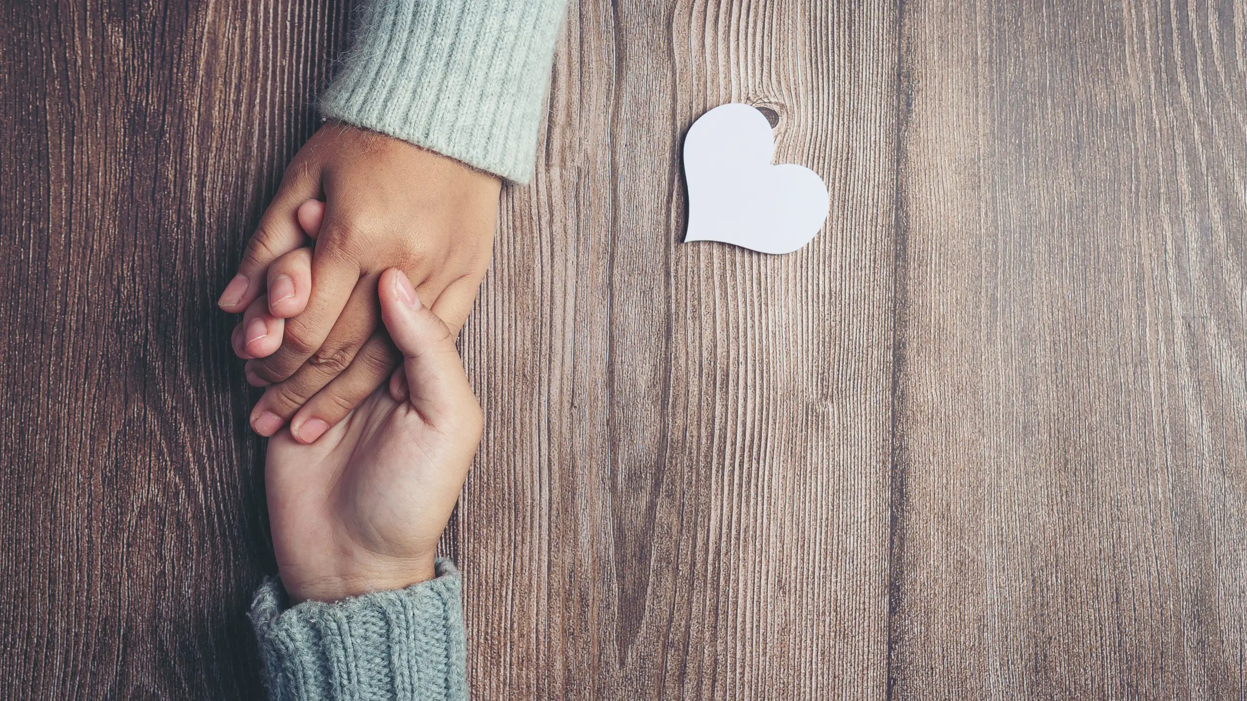 Zwei sich haltende Hände und ein Herz, das auf einem Tisch liegt